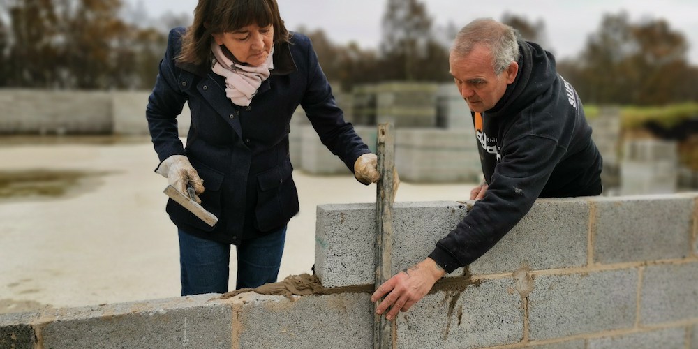 Woman and male working on wall of bricks for construction of a Buddhist Temple in the UK.