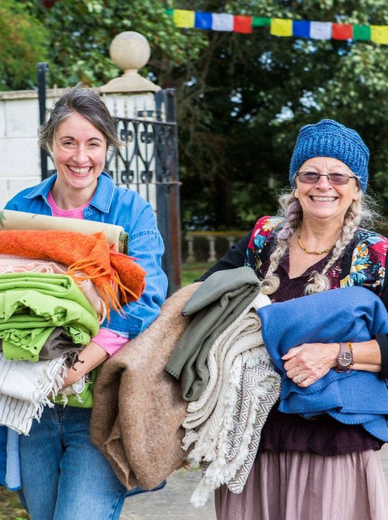 Two broadly smiling woman carrying bedlinen.