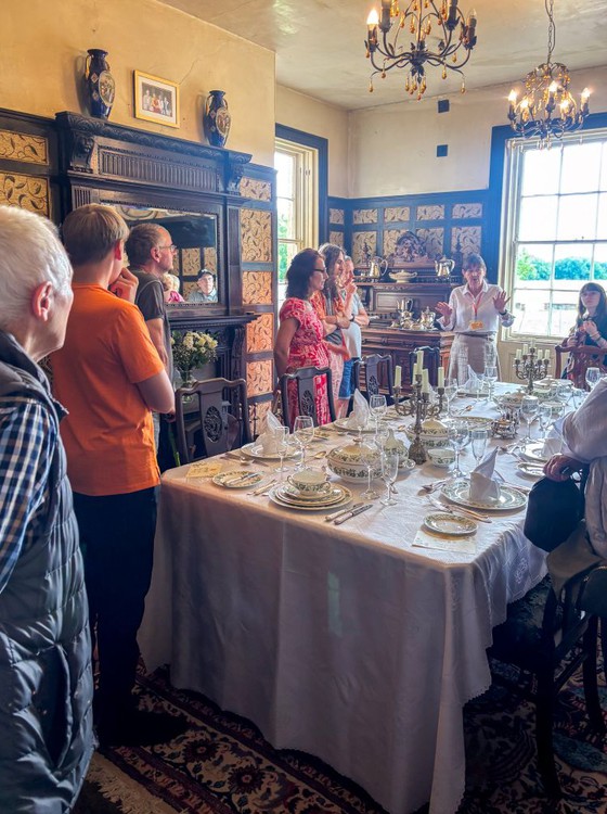 Group of people around a traditionally set dining table during a heritage tour at Lindholme Hall.