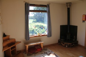 Photograph of the inside of a Gomde retreat hut. A wood-burning stove and a window looking out onto a forest are visible.