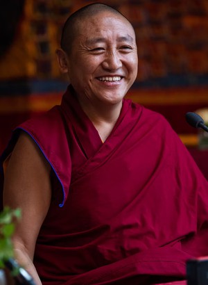 Smiling Buddhist monk and teacher, Lama Oser, in maroon robes.