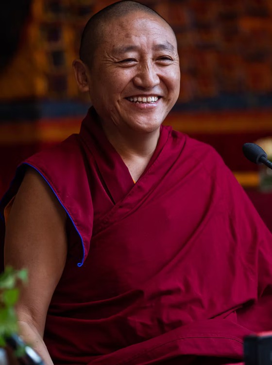 Smiling Buddhist monk and teacher, Lama Oser, in maroon robes.