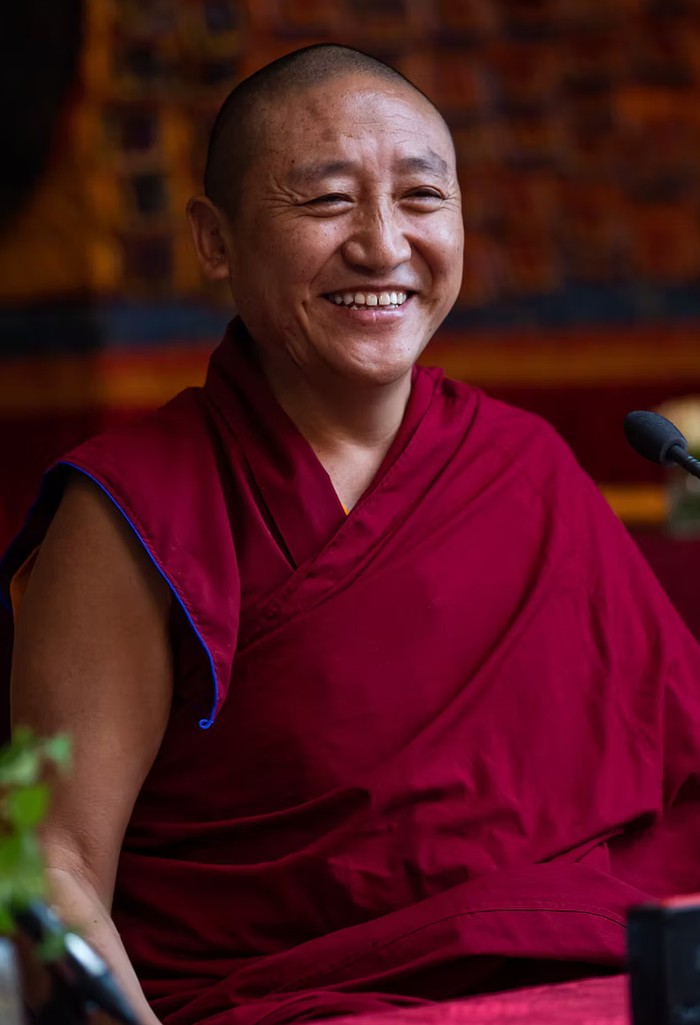 Smiling Buddhist monk and teacher, Lama Oser, in maroon robes.