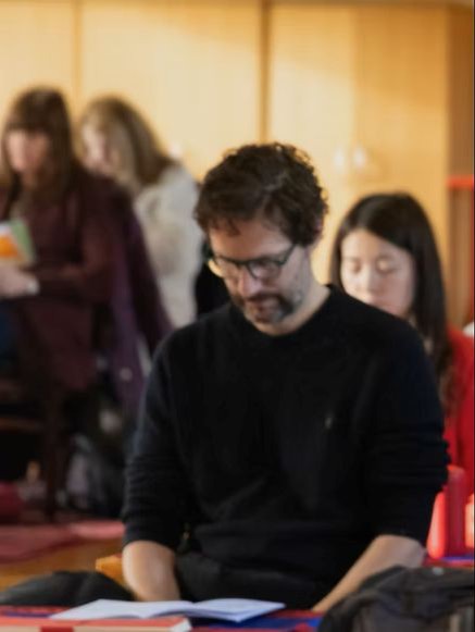 A male Buddhist meditation practitoner with a dharma text in front of him.