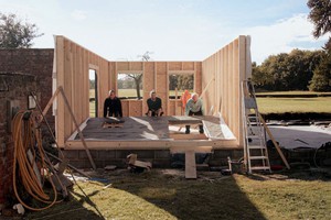Men standing within the wooden walls of a newly build Buddhist meditation retreat cabin.