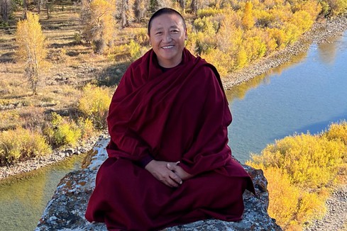 Buddhist monk sitting on a rock overlooking a valley and a river.