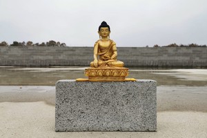 Golden Buddha statue on top of pile of bricks to be used to build a Buddhist Temple in the UK.