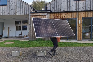 Volunteer carrying solar panel for carbon neutral strategy at Buddhist Retreat Centre England.