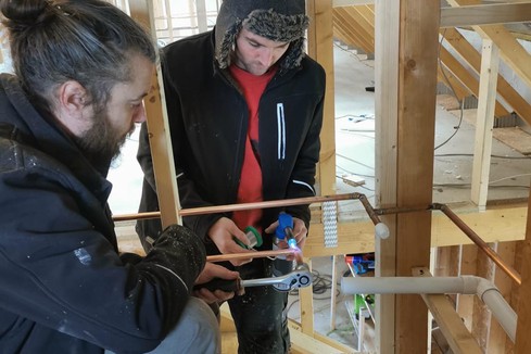 Two men soldering and doing building work at peatland meditation retreat rooms