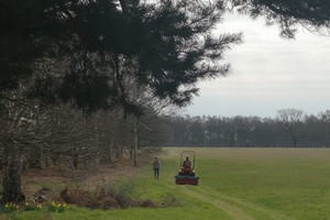 Two people in the fields of Gomde UK mowing grass, volunteering at Buddhist centre